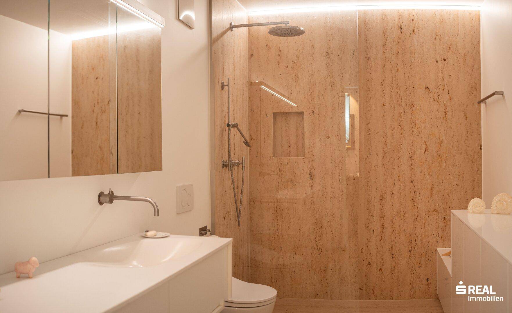 Stilvolles Badezimmer mit begehbarer Dusche, Natursteinfliesen und einem modernen Waschtisch mit integriertem Spiegel.