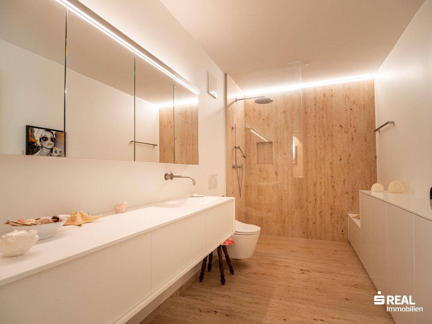 Modernes Badezimmer mit langer Waschtischplatte, integriertem WC und einer geräumigen begehbaren Dusche mit Natursteinoptik.