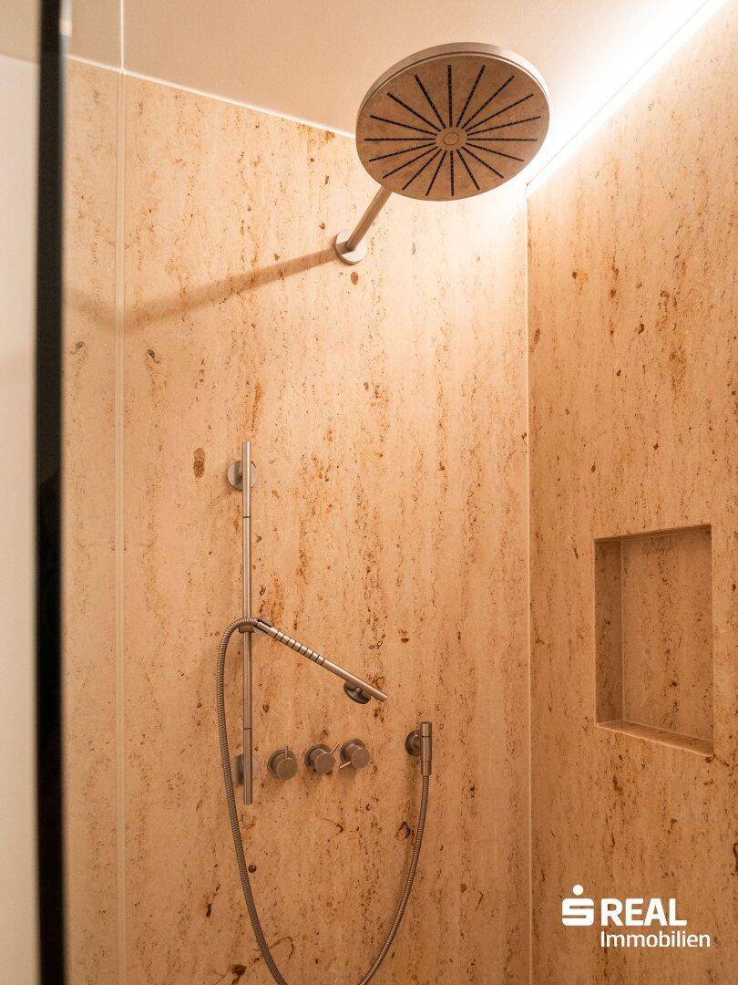 Detailaufnahme einer modernen Regendusche mit Natursteinfliesen und eleganten Armaturen im Badezimmer.