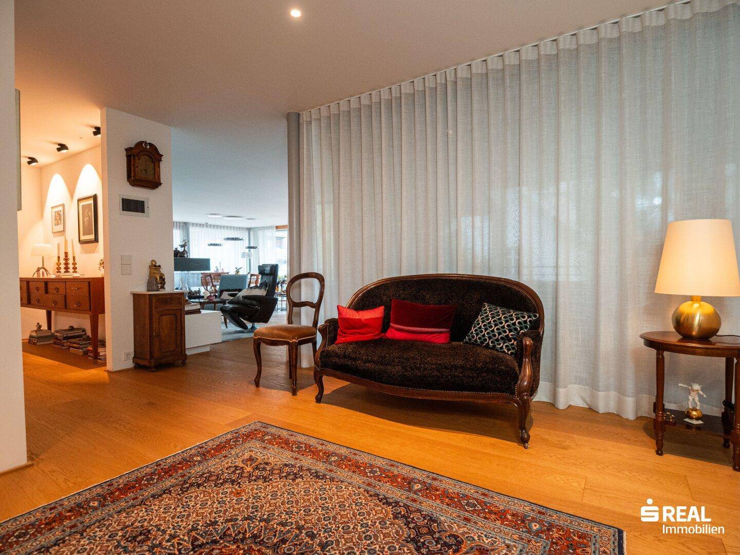Geräumiges Wohnzimmer mit elegantem Sofa, Holzboden und großen Fenstern, die viel Licht hereinlassen.