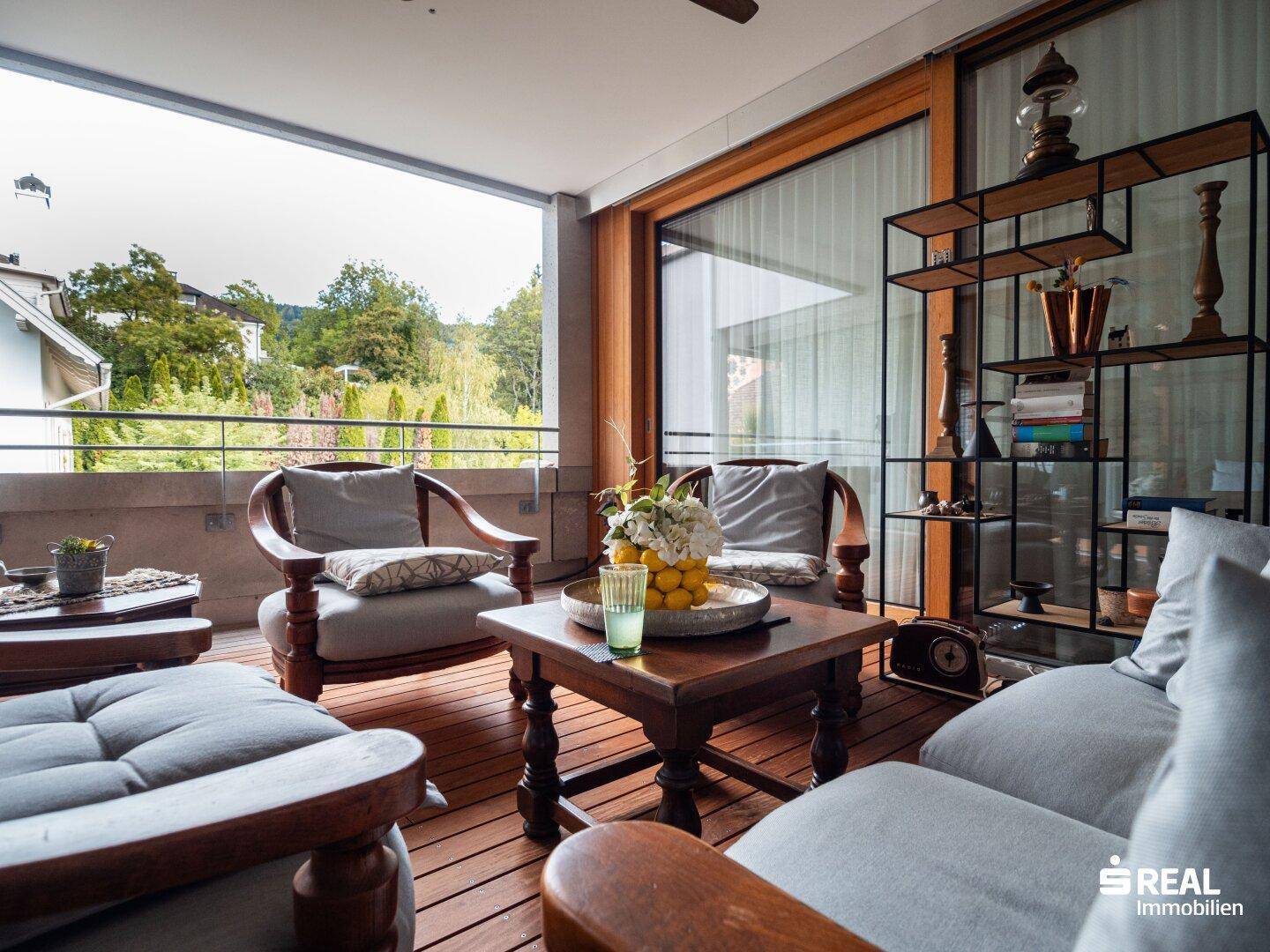 Gemütlicher Balkon mit Holzboden und bequemen Sitzmöbeln, umgeben von Bäumen.