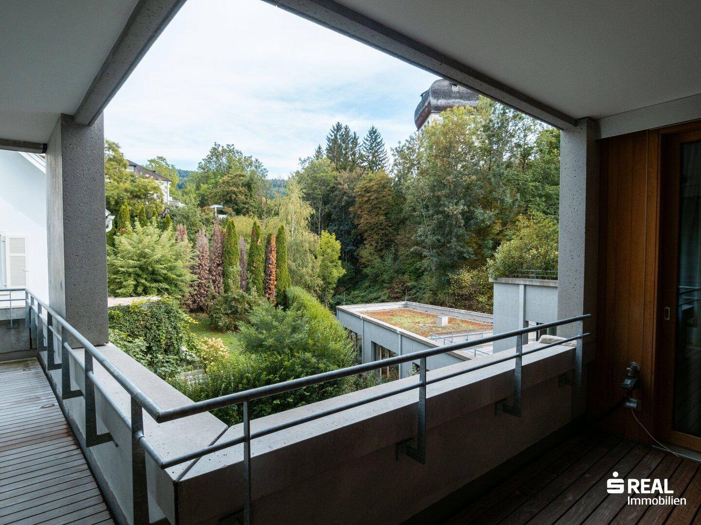 Geräumiger Balkon mit Holzboden und Blick auf einen grünen Garten und die umliegende Natur.