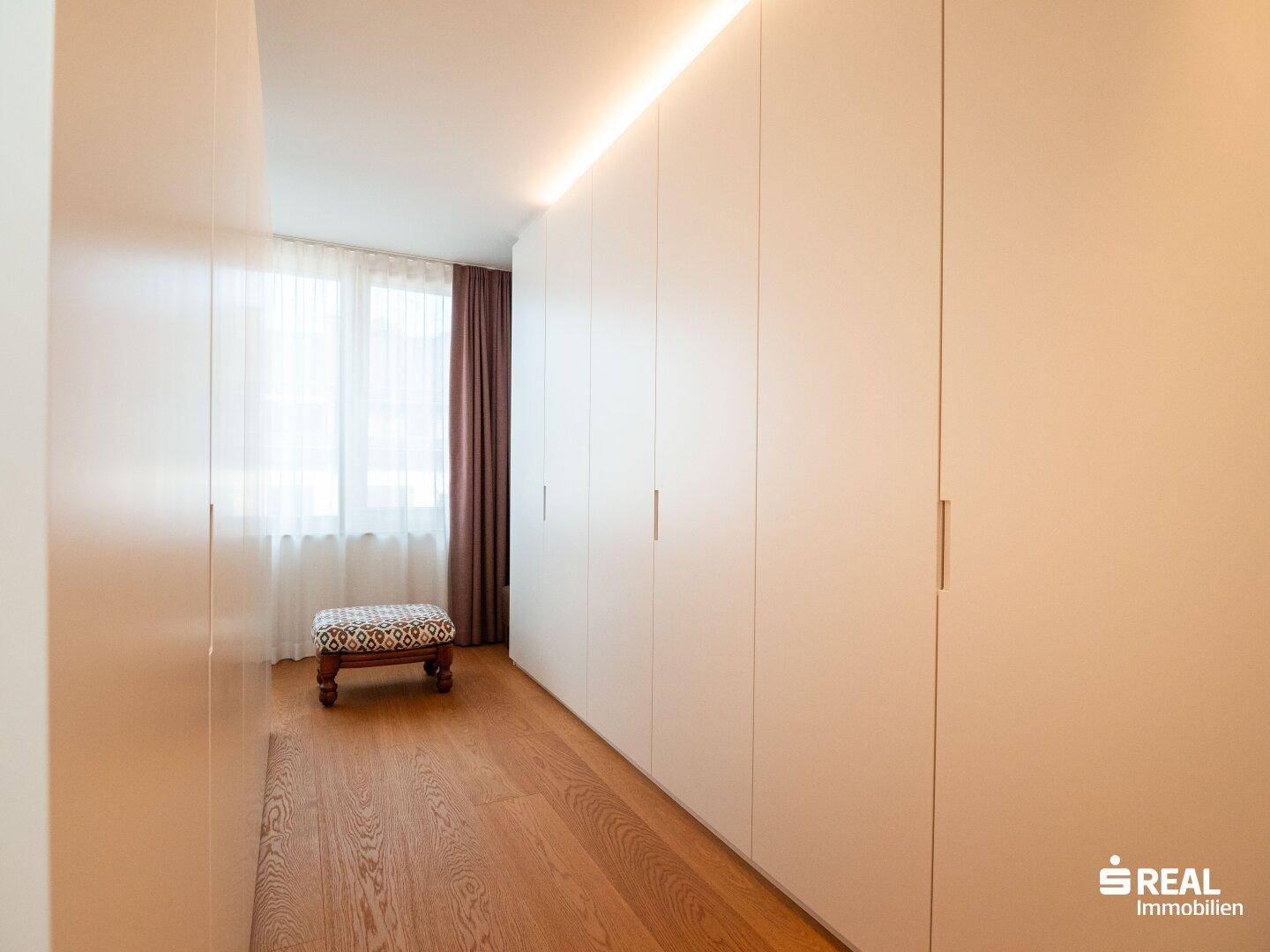 Heller Ankleidebereich mit raumhohen Einbauschränken und einem Fenster, das viel Tageslicht hereinlässt.