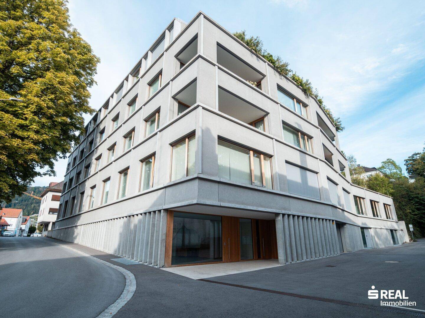 Modernes Mehrfamilienhaus mit Betonfassade und großen Fenstern in städtischer Umgebung.