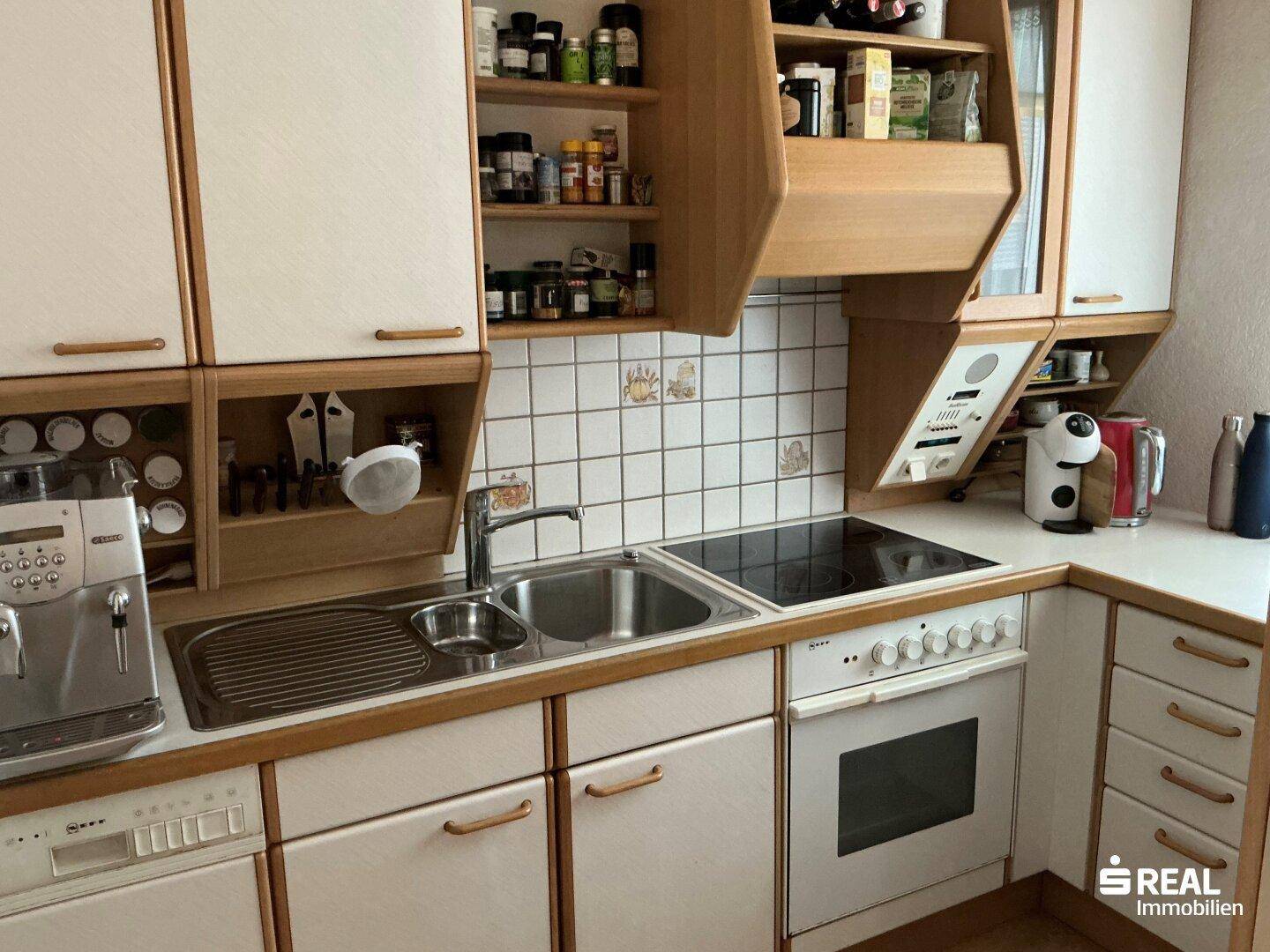 Funktionale Küche mit hellen Holzfronten, Einbaugeräten und gefliestem Fliesenspiegel.