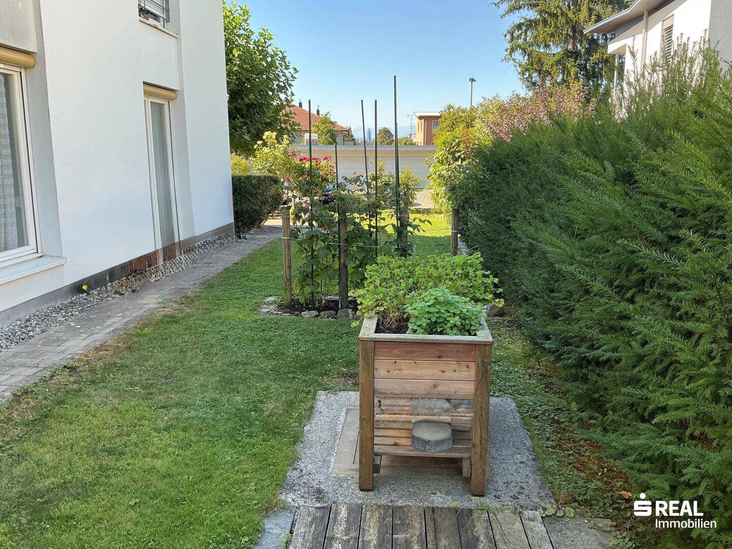 Schmaler Gartenstreifen mit Hochbeet für Kräuter und Sträuchern entlang der Hauswand.