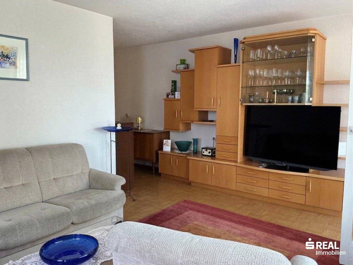 Wohnzimmer mit Holzmöbeln, TV-Schrank und einem beigen Sofa, Blick in den Raum.