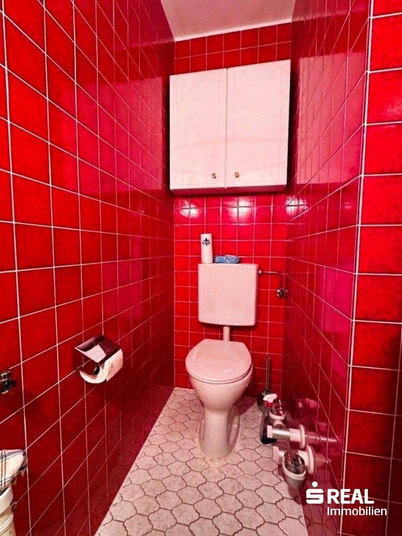 Kleines Gäste-WC mit leuchtend roten Fliesen und weißem Wandschrank.