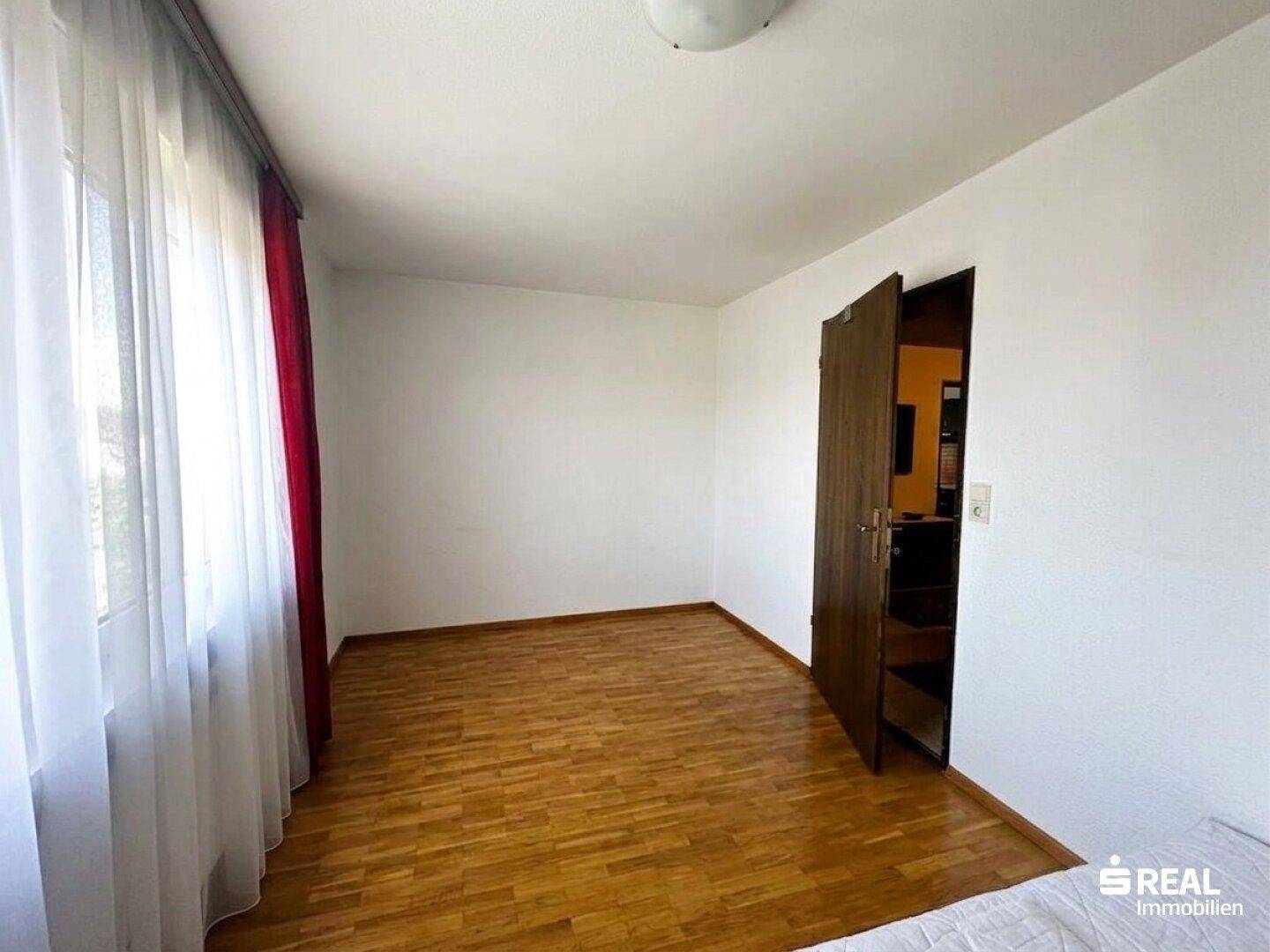 Leeres Schlafzimmer mit hellem Parkettboden und großen Fenstern, bereit zur Einrichtung.