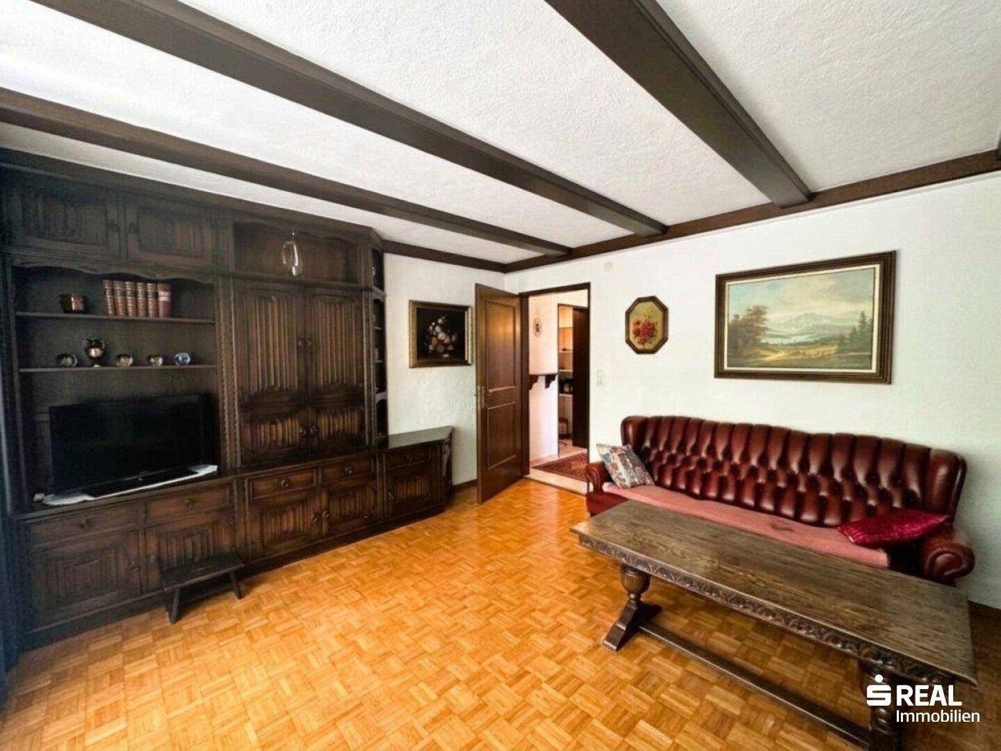 Traditionelles Wohnzimmer mit Holzbalkendecke, Parkettboden und klassischer Ledercouch.