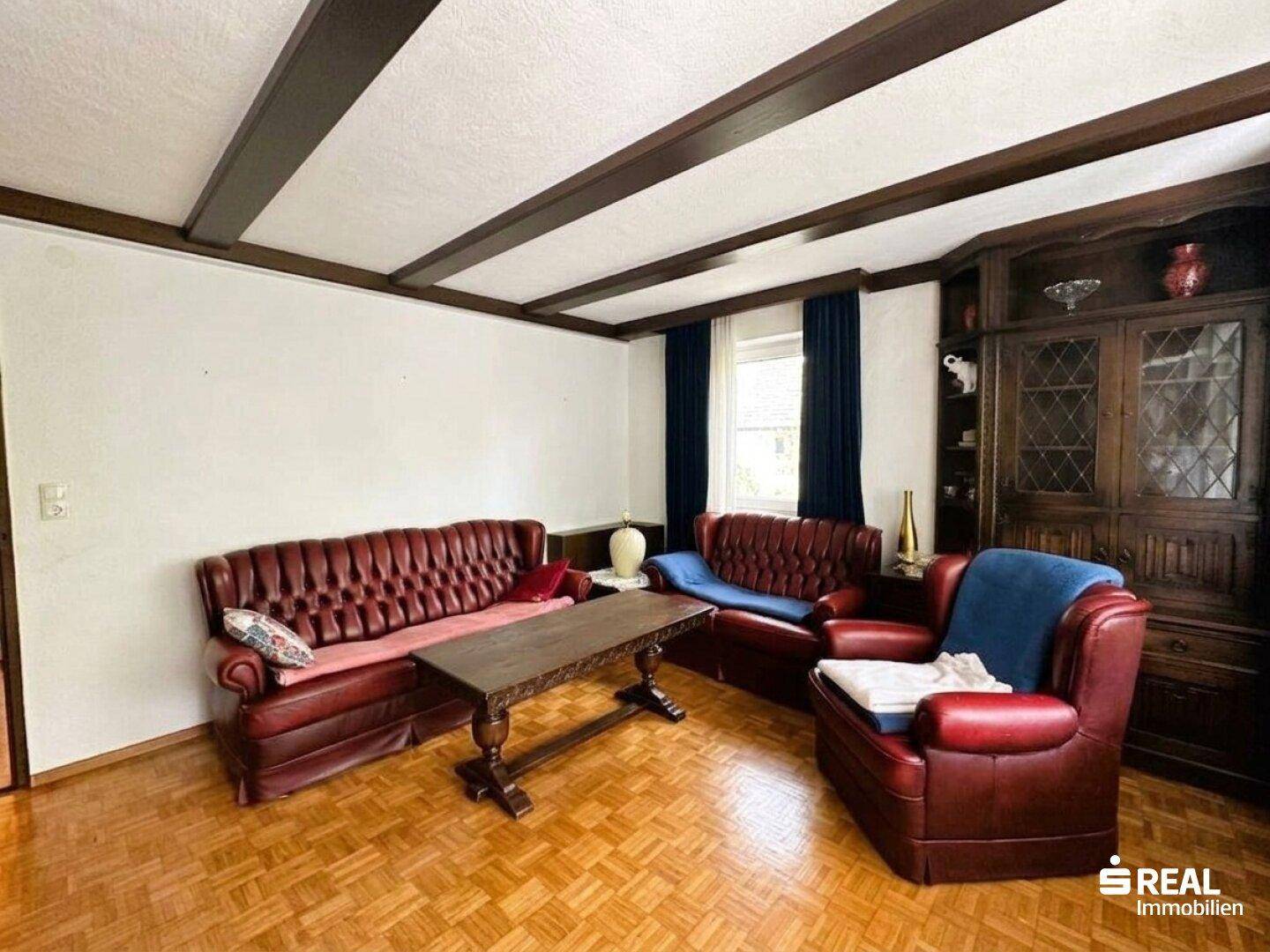 Geräumiges Wohnzimmer mit Holzbalkendecke, Parkettboden und bequemen Ledersofas.