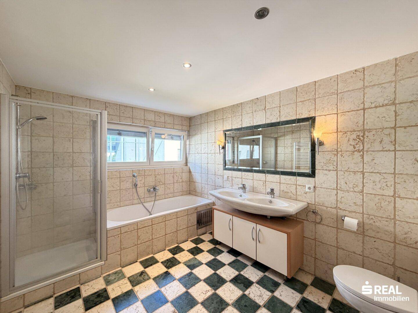 Geräumiges Badezimmer mit Doppelwaschbecken, Badewanne, Dusche und gemusterten Fliesen.
