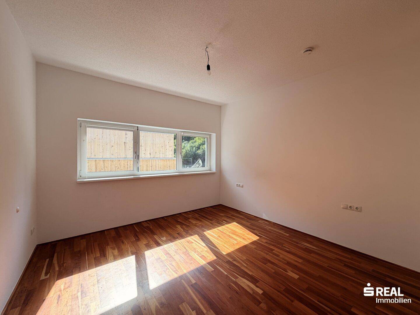 Helles Zimmer mit Holzboden und einem Fenster, das Tageslicht in den Raum bringt.