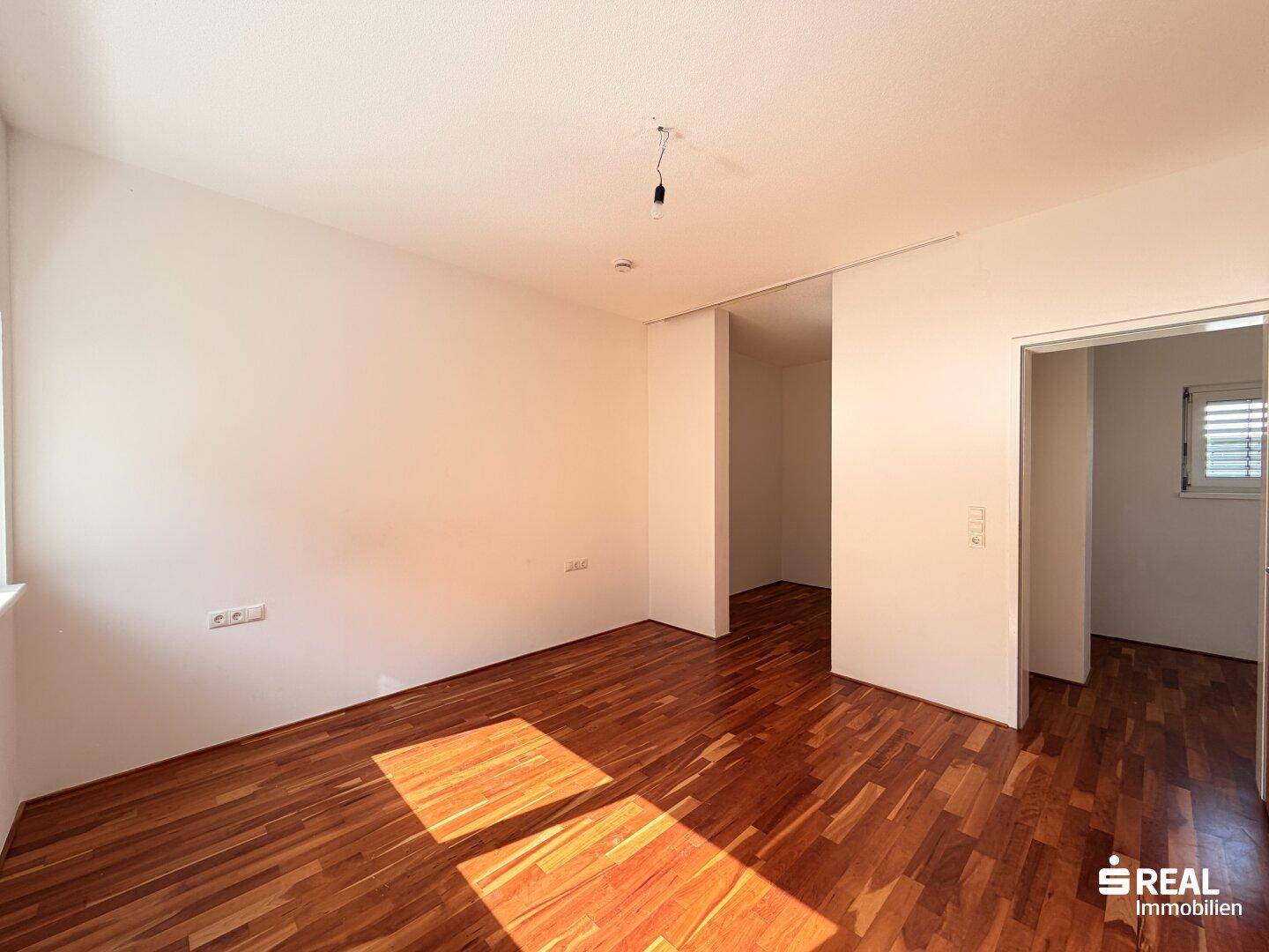 Geräumiges Zimmer mit Holzboden und Schiebetür, die zu einem weiteren Raum führt.