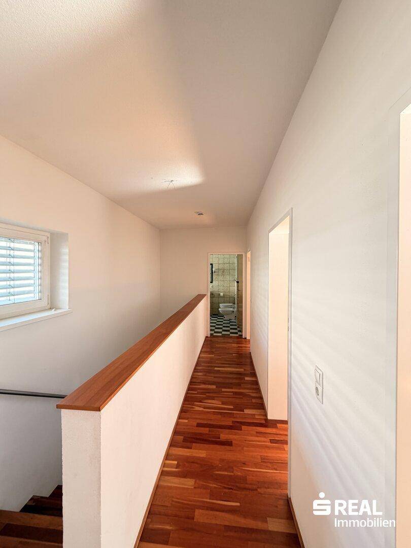 Langer Flur mit Holzboden und Fenster, der zu einem Badezimmer führt.