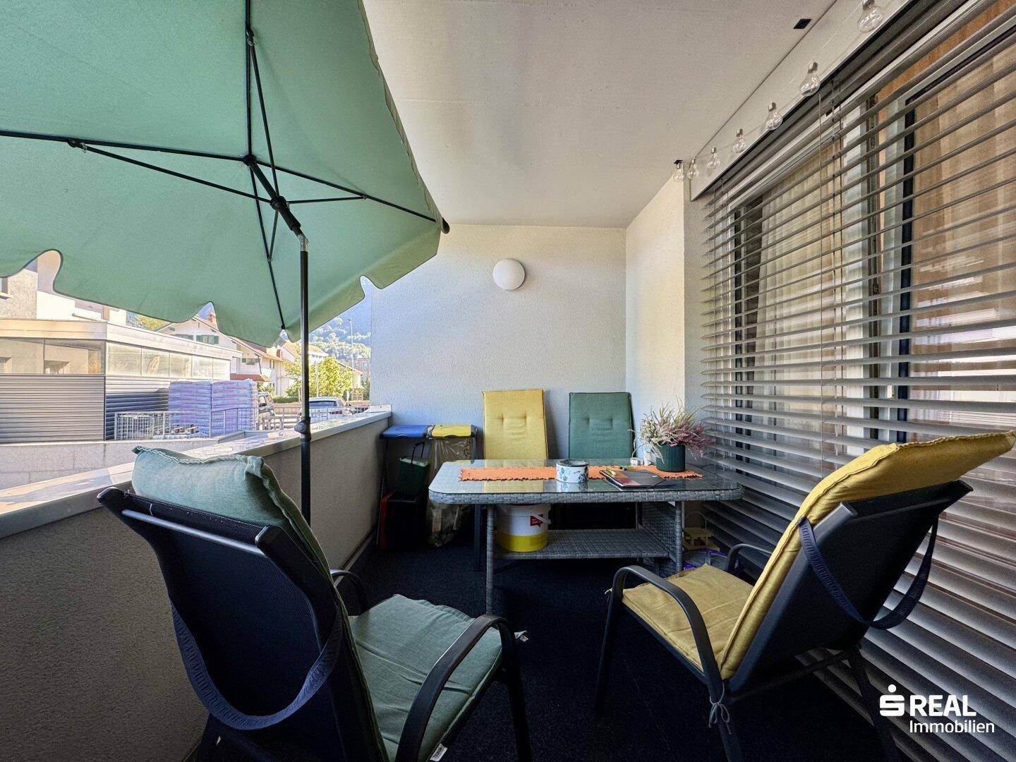 Gemütlicher Balkon mit Sitzgelegenheiten, Sonnenschirm und Blick auf die Umgebung.