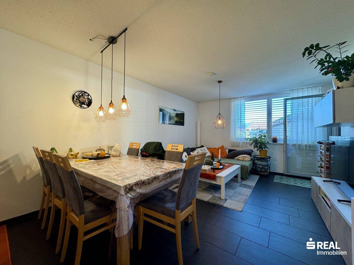 Geräumiger Wohn- und Essbereich mit großem Esstisch und Zugang zum Balkon durch große Fenster.