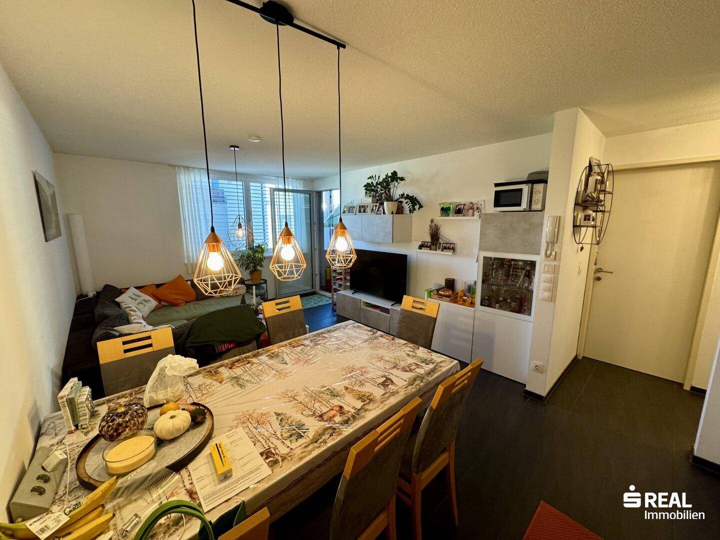 Essbereich mit großem Tisch, moderner Beleuchtung und Blick auf den Wohnbereich und Eingang.