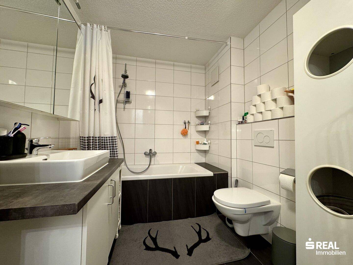 Gefliestes Badezimmer mit Badewanne, WC, Waschbecken und Spiegelschrank.