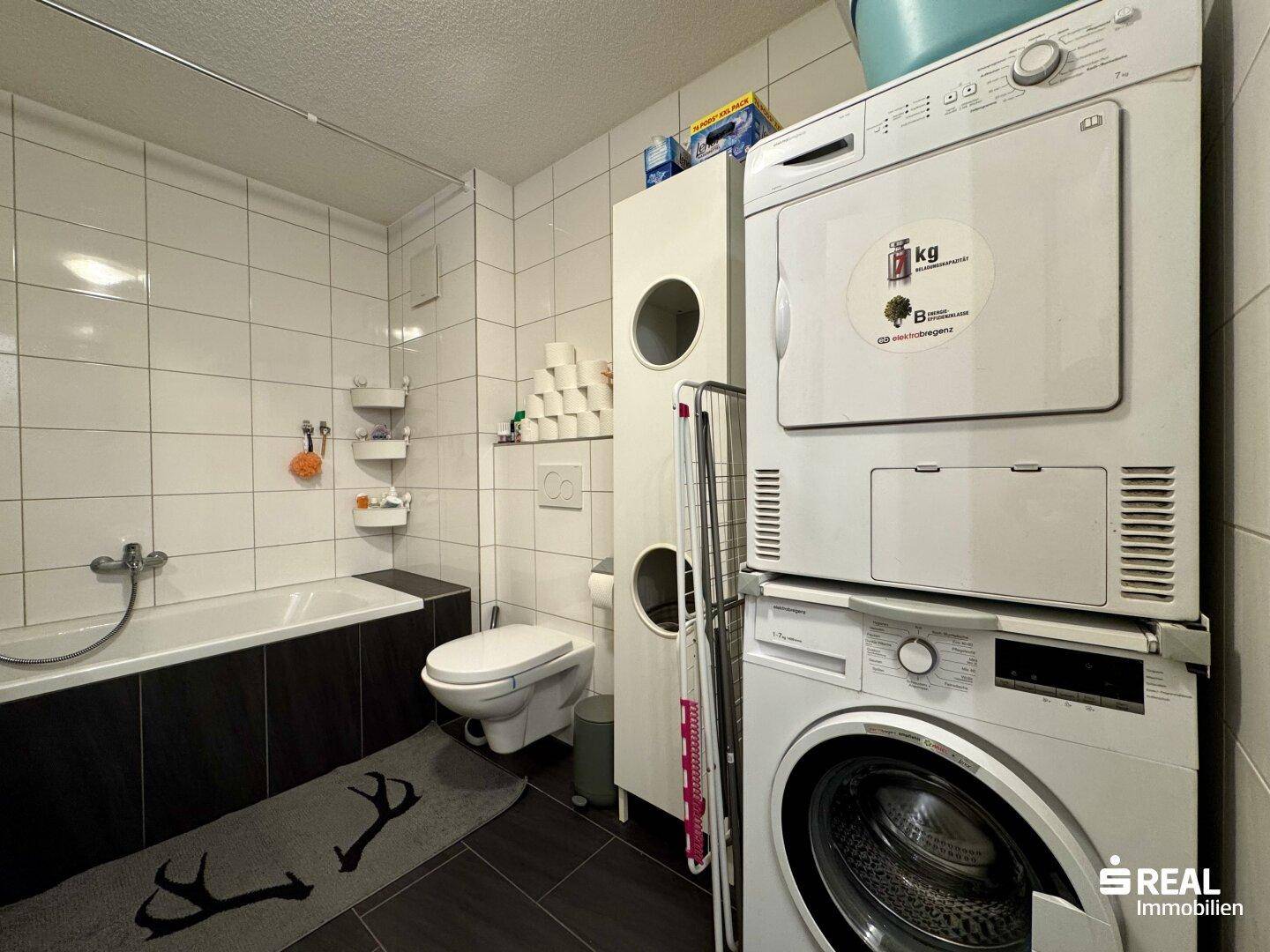Funktionales Badezimmer mit Badewanne, WC, Waschmaschine und Trockner.