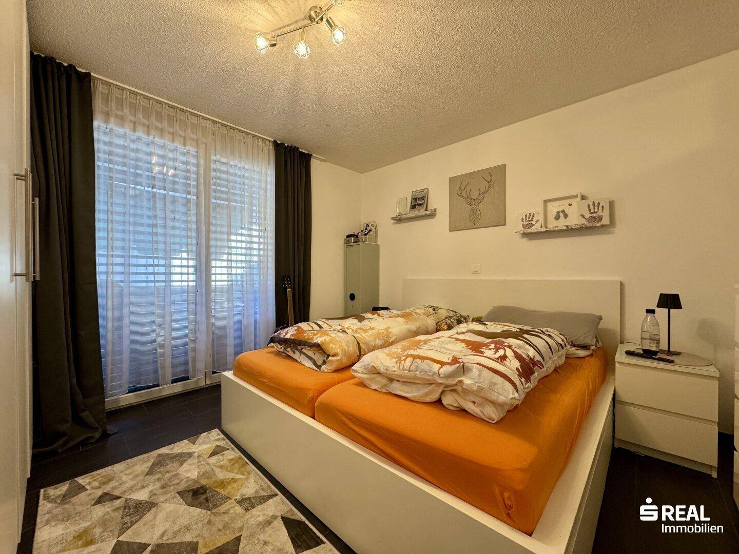 Helles Schlafzimmer mit Doppelbett, dunklem Boden und Zugang zum Balkon.