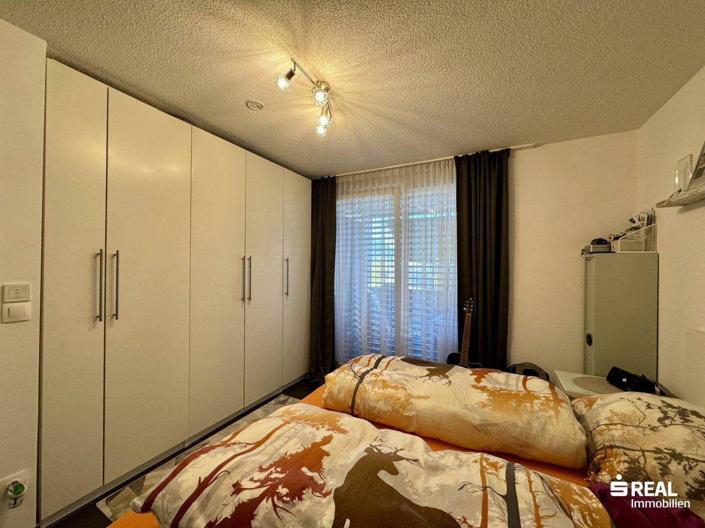 Schlafzimmer mit großen Einbauschränken, Doppelbett und Fenster mit Jalousien.