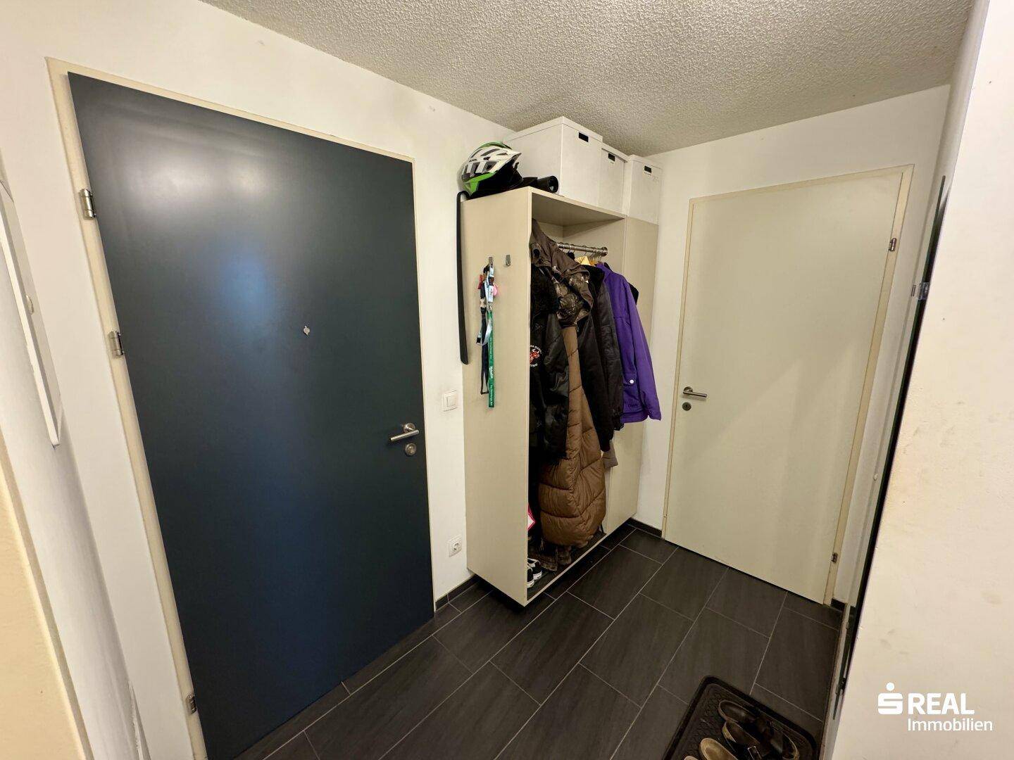 Eingangsbereich mit dunklem Fliesenboden und Garderobenschrank.