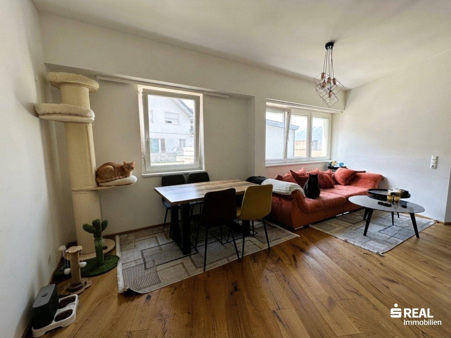 Kombinierter Wohn- und Essbereich mit Esstisch, bequemer Couch und Blick nach draußen durch die Fenster.