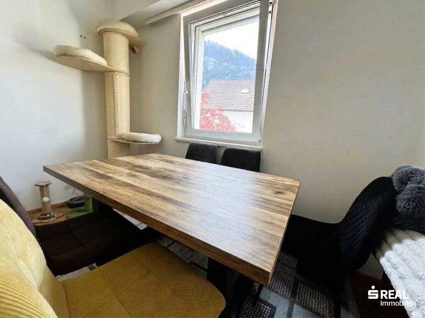 Essbereich mit Holztisch und Stühlen, bietet einen schönen Blick auf die umliegende Landschaft durch das Fenster.