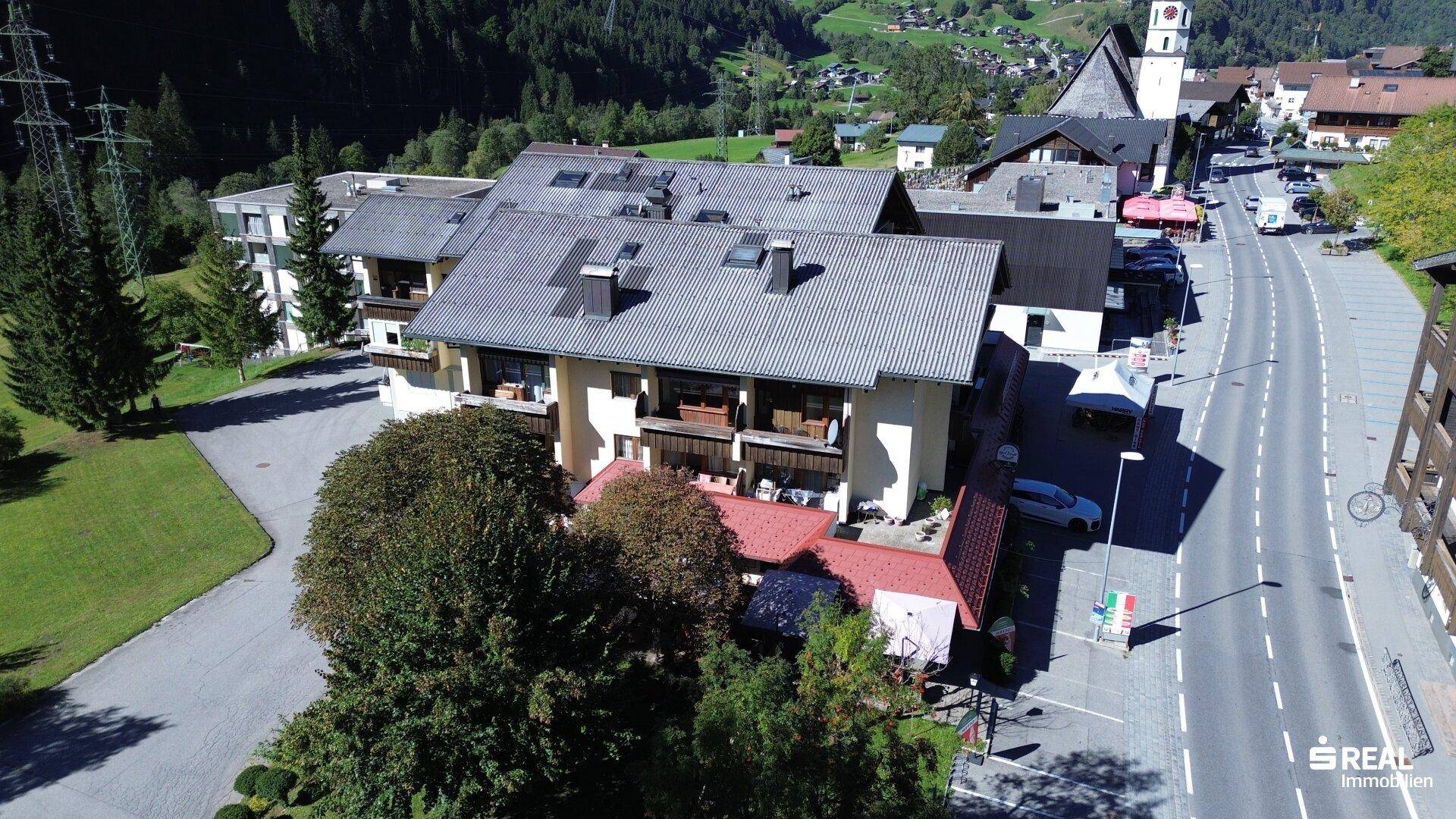 Luftaufnahme einer Gebäudegruppe entlang einer Straße in einem alpinen Tal.