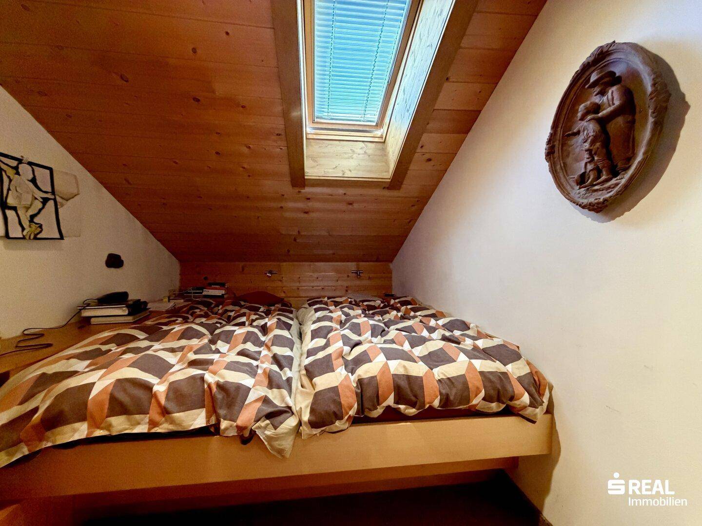 Schlafzimmer im Dachgeschoss mit Holzverkleidung, zwei Einzelbetten und Dachfenster für natürliches Licht.