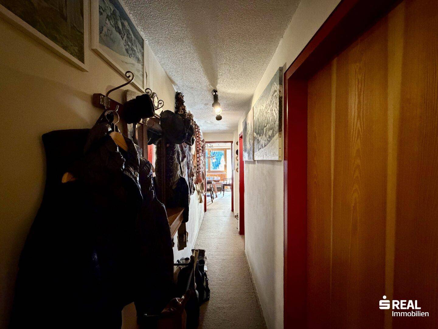 Langer Flur mit Garderobe und Holztüren, der einen Blick in den Wohnbereich ermöglicht.