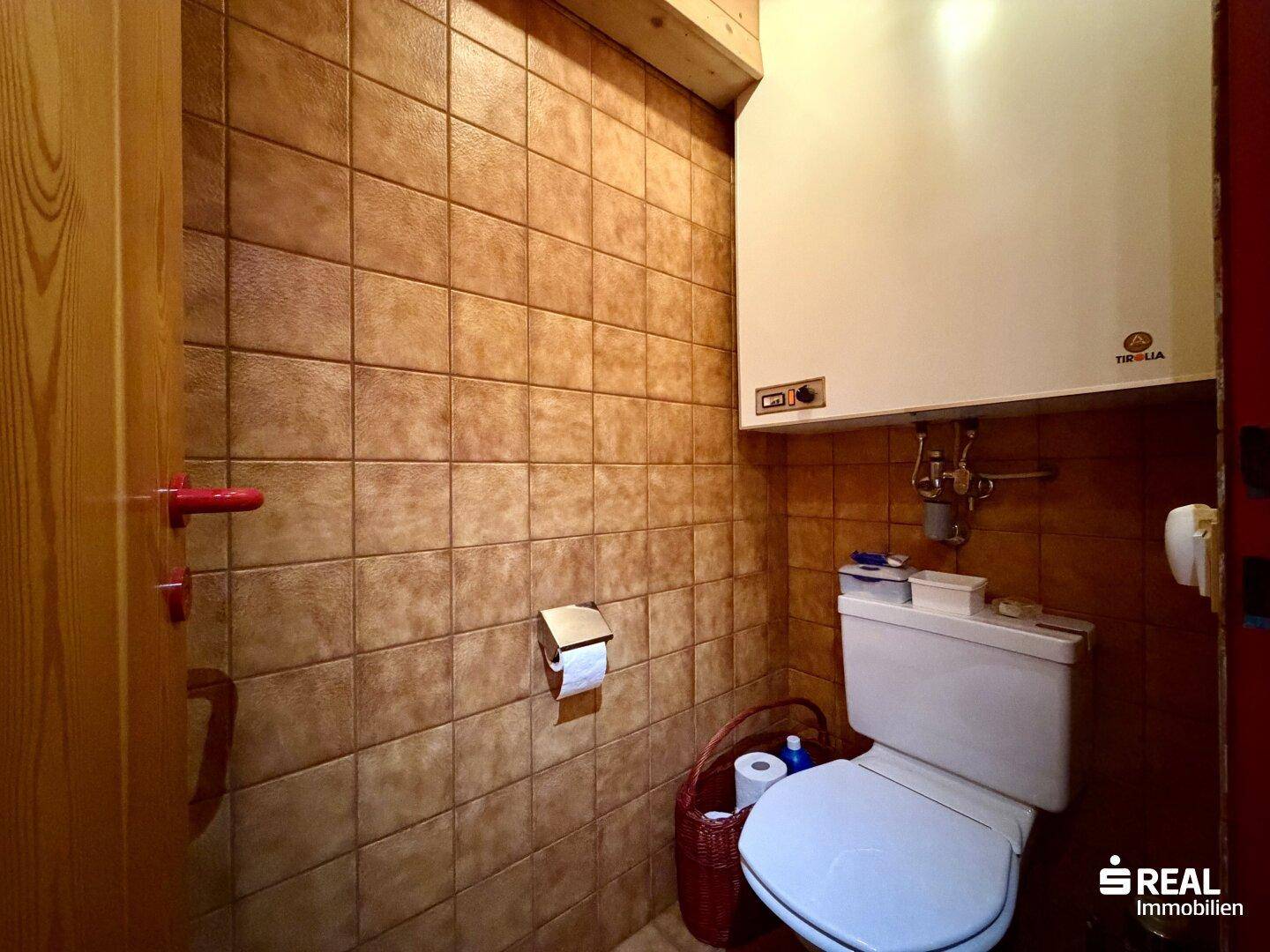 Separate Toilette mit braunen Wandfliesen und einem Wand-WC.