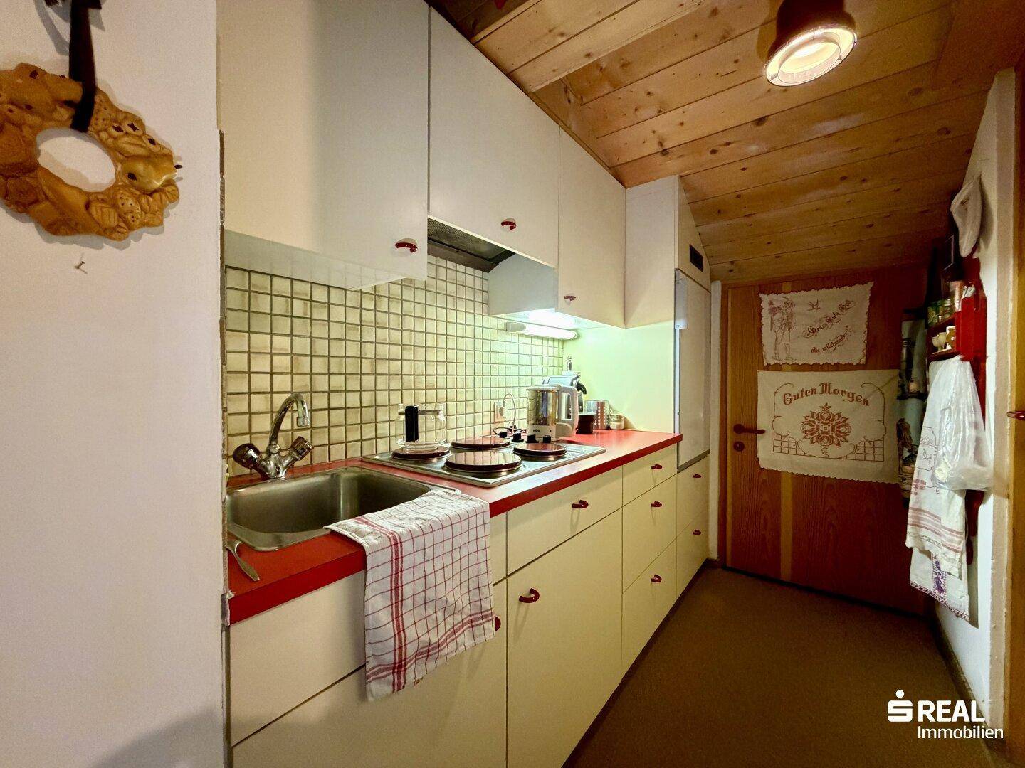 Kleine Küche im Landhausstil mit weißen Schränken, roter Arbeitsplatte und Holzdecke.