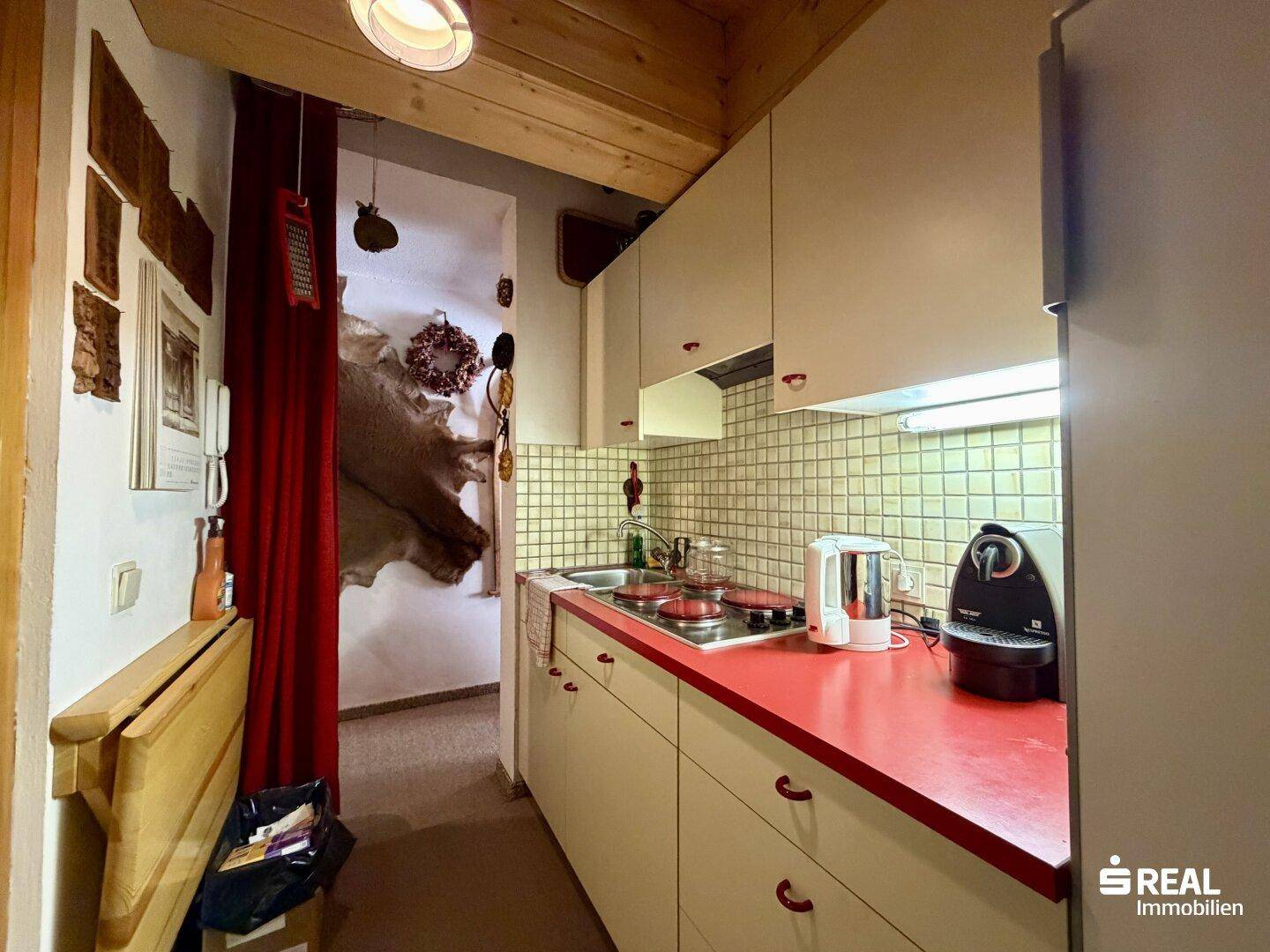 Funktionale Küchenzeile mit hellen Fronten, integrierten Geräten und rustikaler Holzdecke.