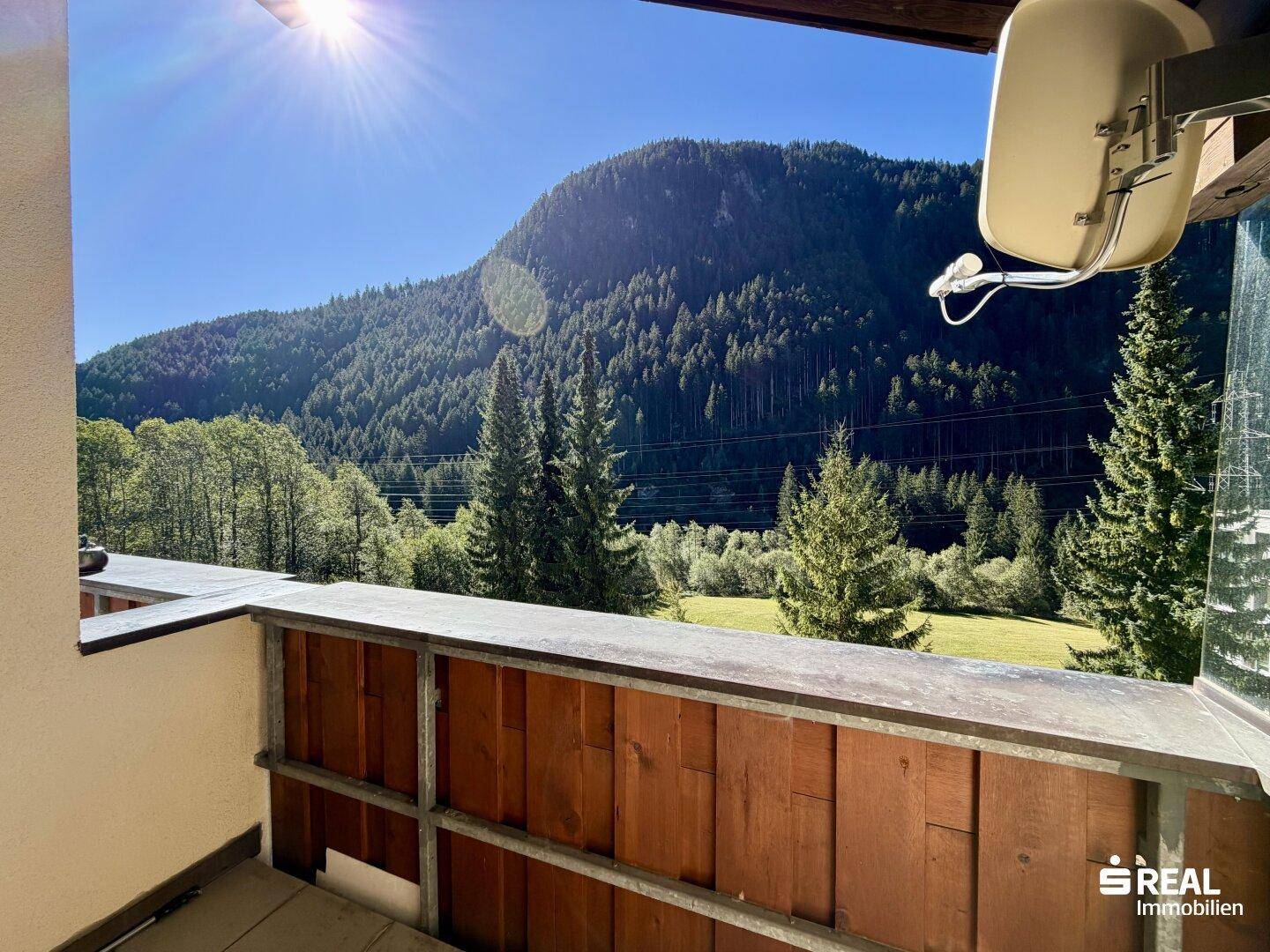 Sonniger Balkon mit Holzelementen und weitem Blick auf die umliegende Berglandschaft.