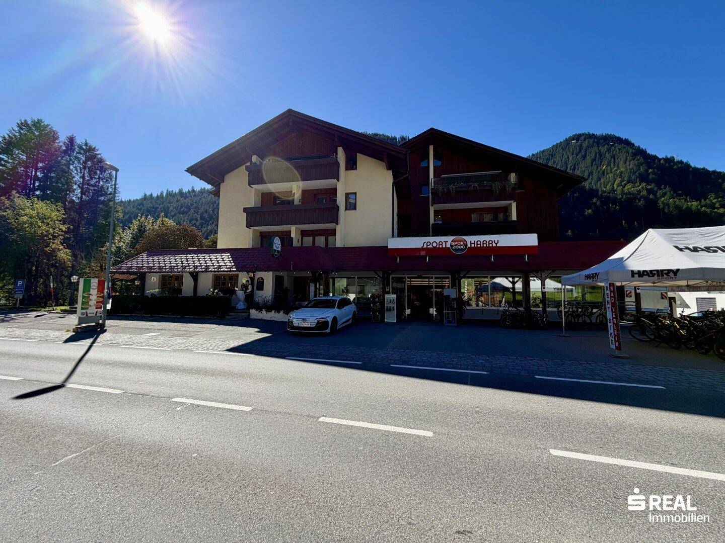 Gebäude mit Geschäftsfront im Erdgeschoss und Wohnungen darüber, an einer Hauptstraße gelegen.