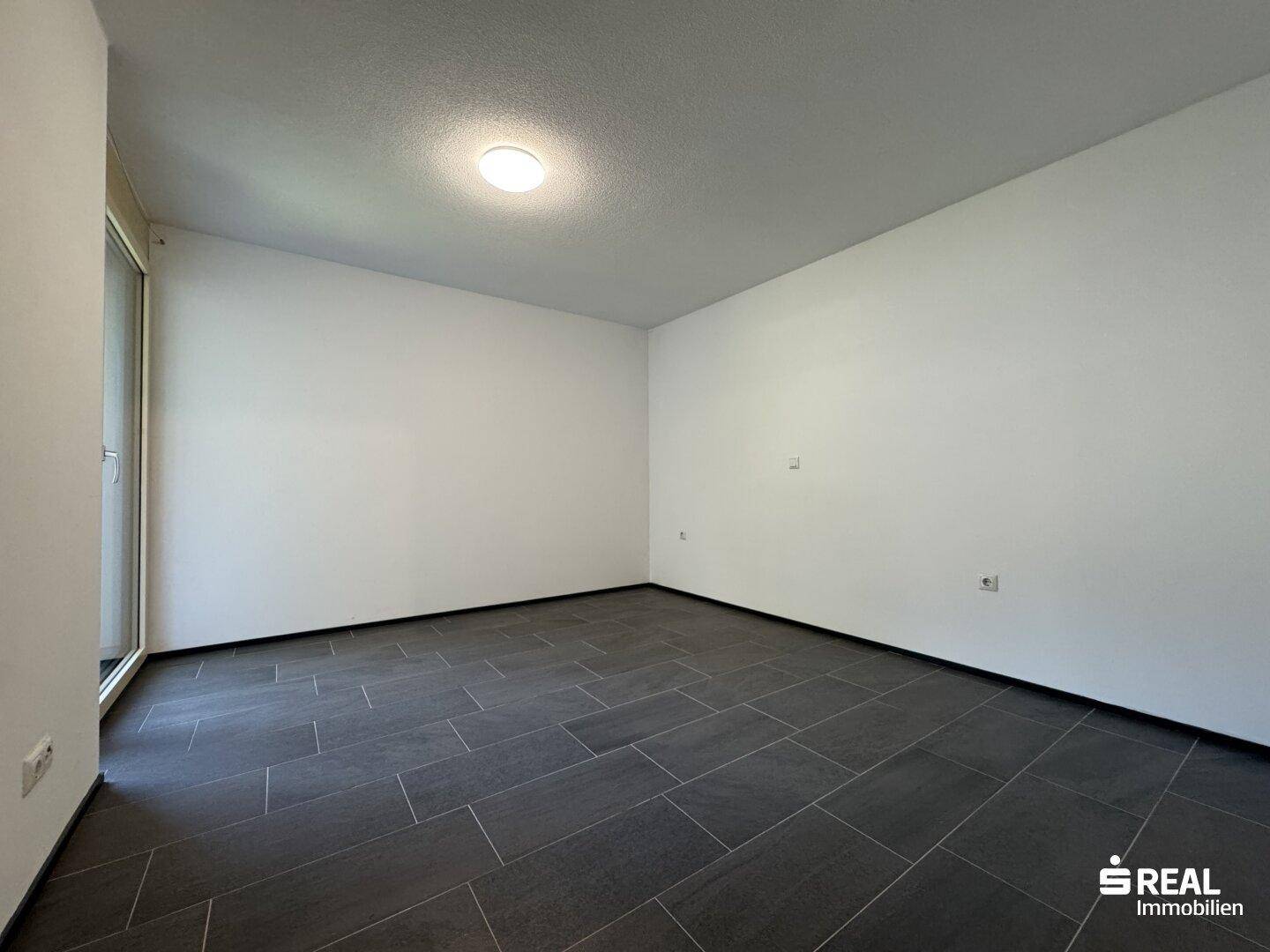 Geräumiges Zimmer mit dunklem Fliesenboden und hellen Wänden, bereit zur individuellen Gestaltung.