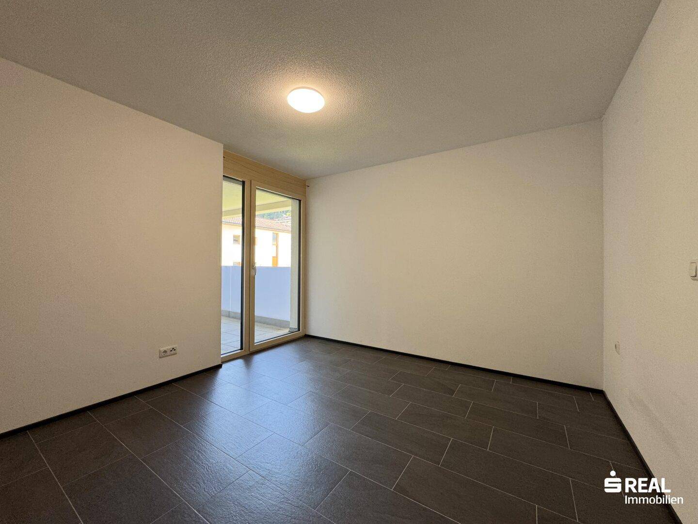 Helles Zimmer mit dunklem Fliesenboden und direktem Zugang zu einem Balkon oder einer Terrasse.