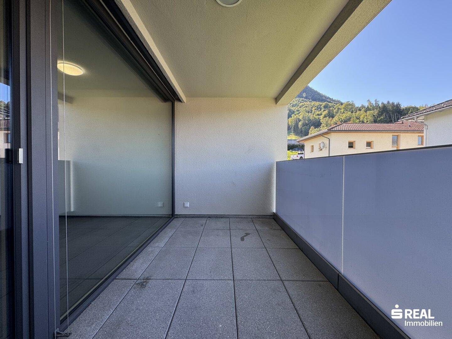 Geräumiger Balkon mit Fliesenboden und weitem Blick auf die umliegende Natur und Berge.