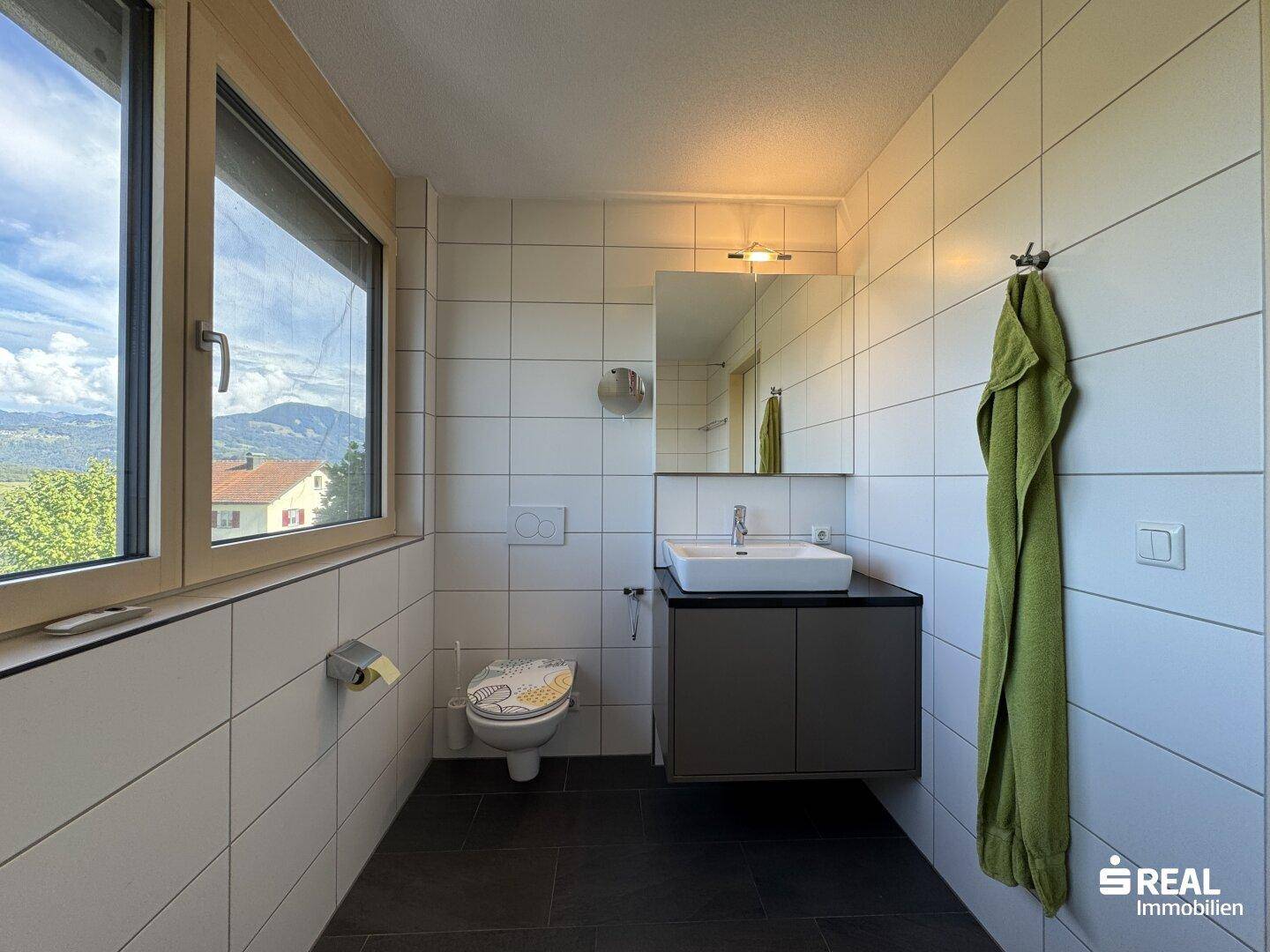 Modernes Badezimmer mit weißen Fliesen, Einzelwaschbecken und Fenster mit Bergblick.