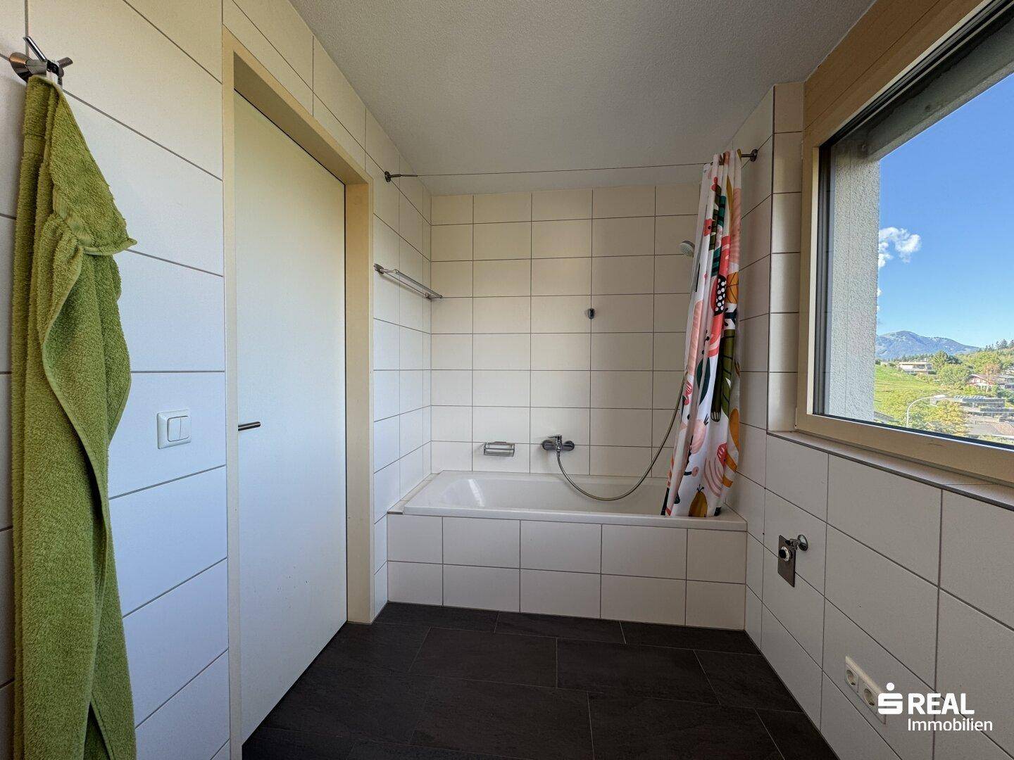 Badezimmer mit Badewanne, weißen Wandfliesen und Fenster für natürliche Belüftung und Licht.