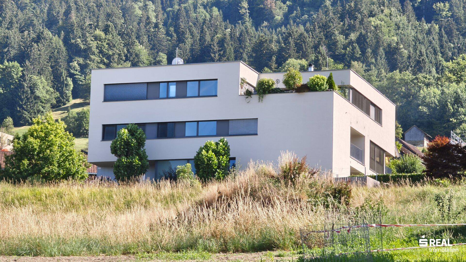 Modernes Wohngebäude in ländlicher Umgebung, umgeben von Feldern und bewaldeten Hügeln.