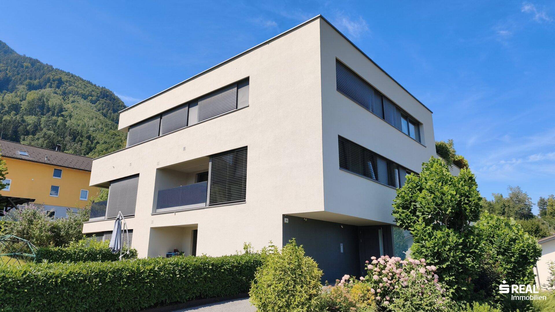 Attraktive Außenansicht des modernen Gebäudes mit gepflegter Bepflanzung und klarem Himmel.