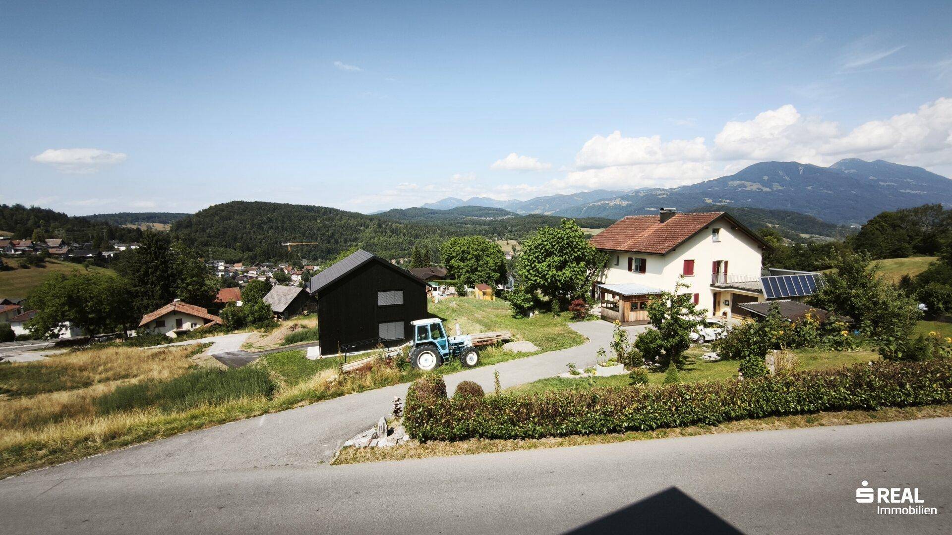 Malerische ländliche Landschaft mit verstreuten Häusern, Feldern und einer beeindruckenden Bergkulisse.