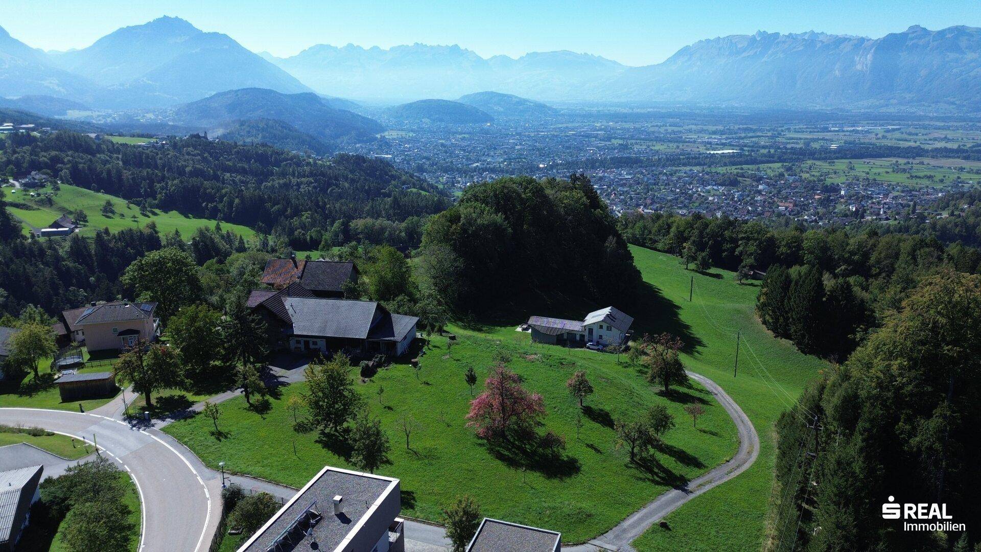 Panoramablick über die ländliche Umgebung mit dem Anwesen, einer Stadt im Tal und den majestätischen Bergen.