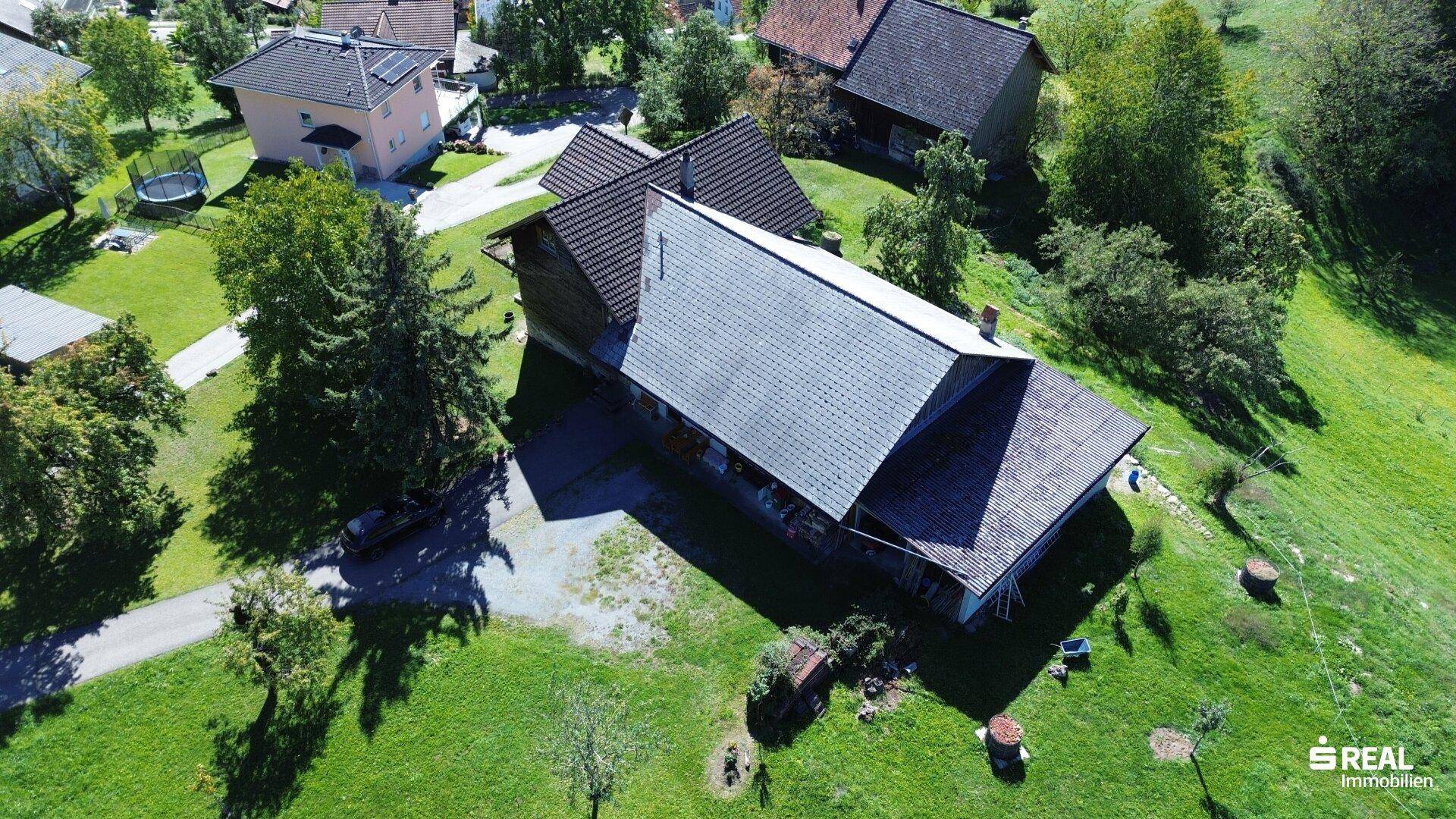 Nahaufnahme eines traditionellen Hauses mit markantem Dach und weitläufigem Grünbereich aus der Vogelperspektive.