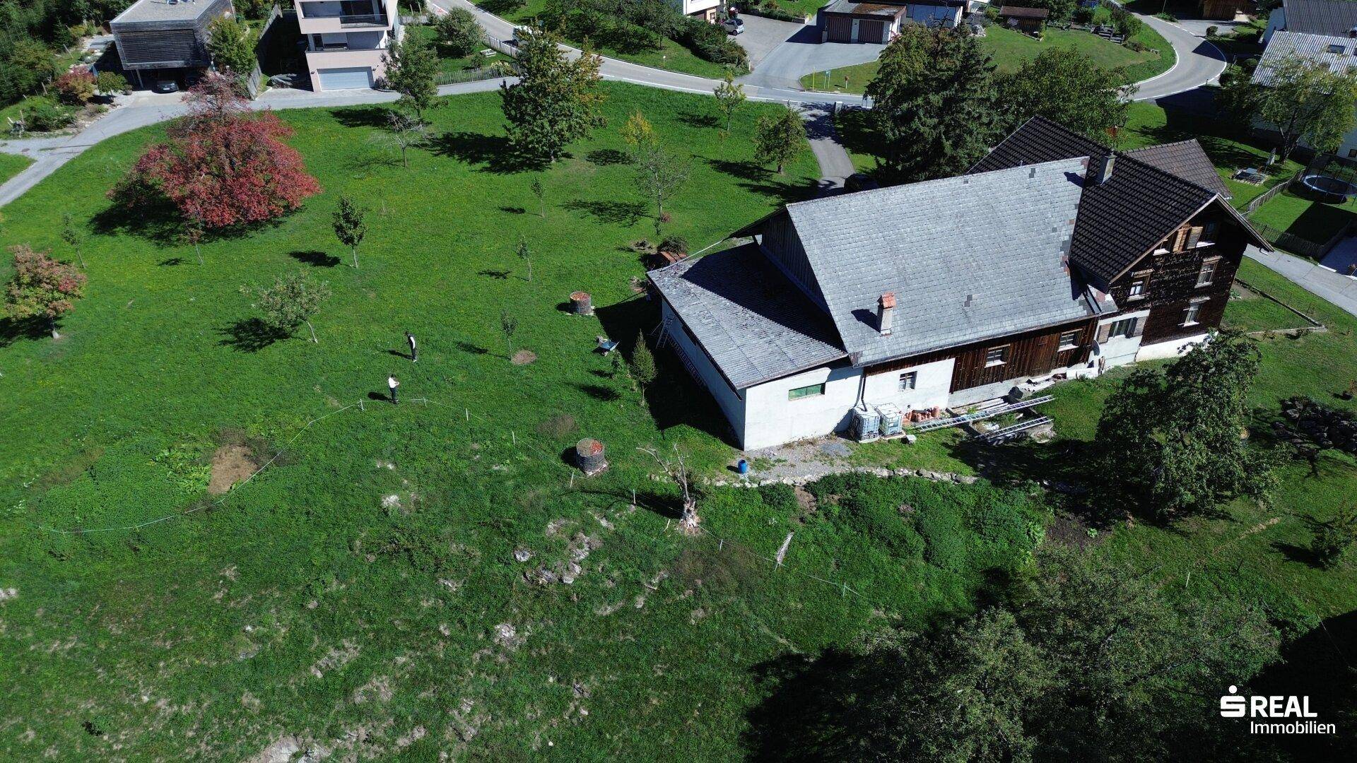 Nahaufnahme des Hauses mit Anbau und dem weitläufigen Gartenbereich, eingebettet in die grüne Umgebung.