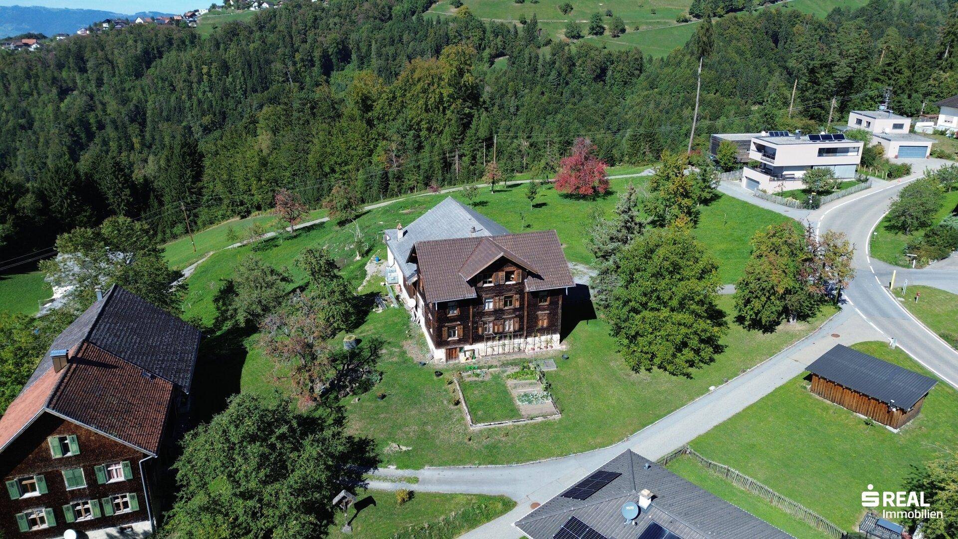 Luftaufnahme zweier traditioneller Häuser mit Gärten, eingebettet in eine grüne Landschaft mit weiteren Gebäuden.