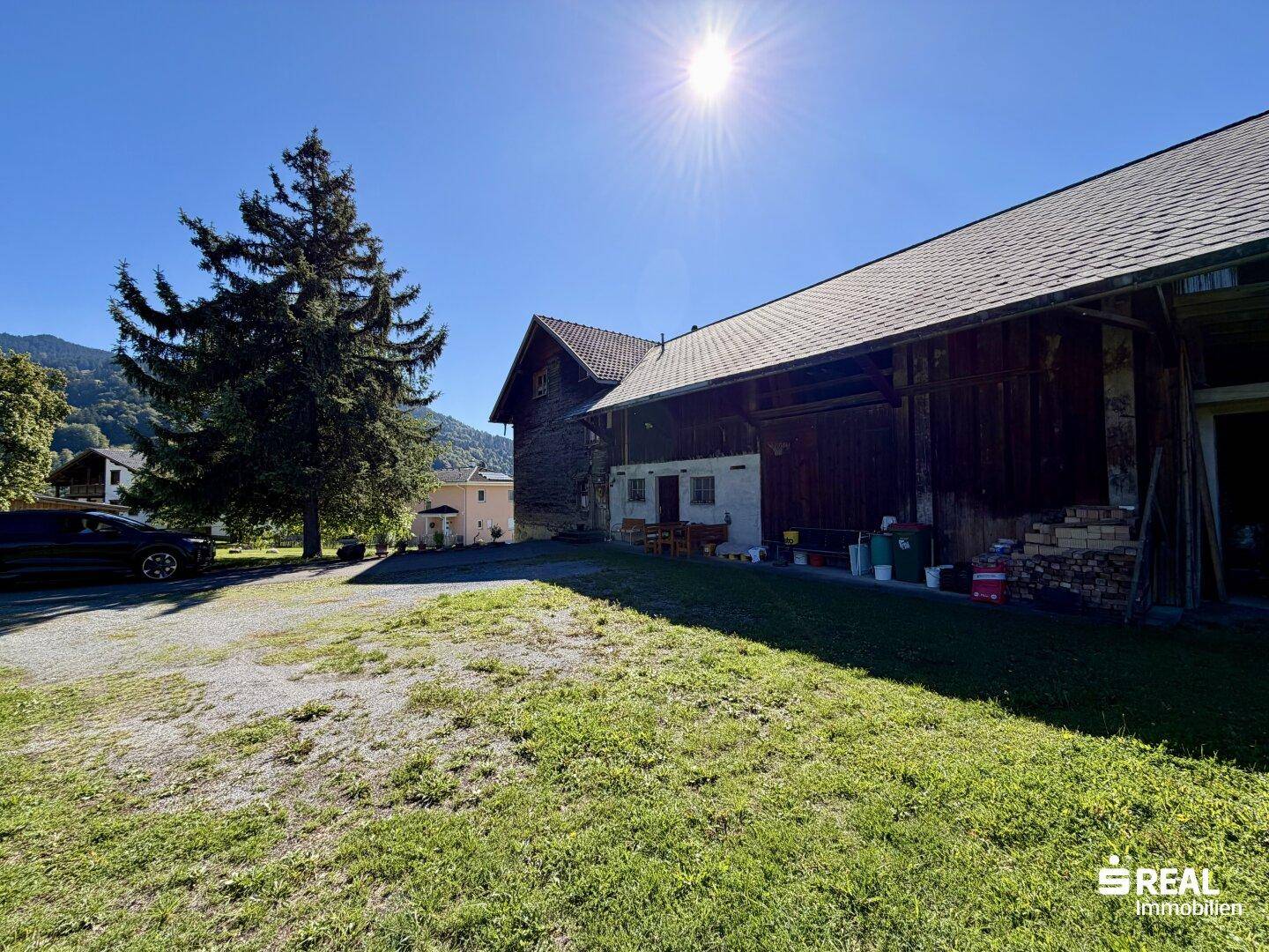 Seitenansicht des Hauses mit angrenzendem Scheunenteil, umgeben von einer Kiesauffahrt und grüner Wiese.